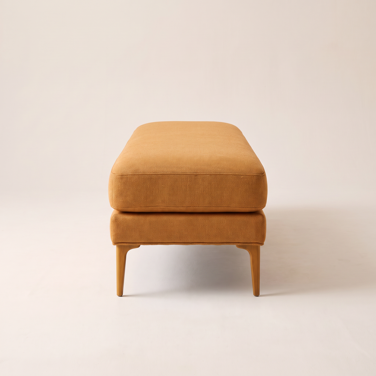 Amber Muse ottoman bench, end view showing the cushion over base and splayed legs
