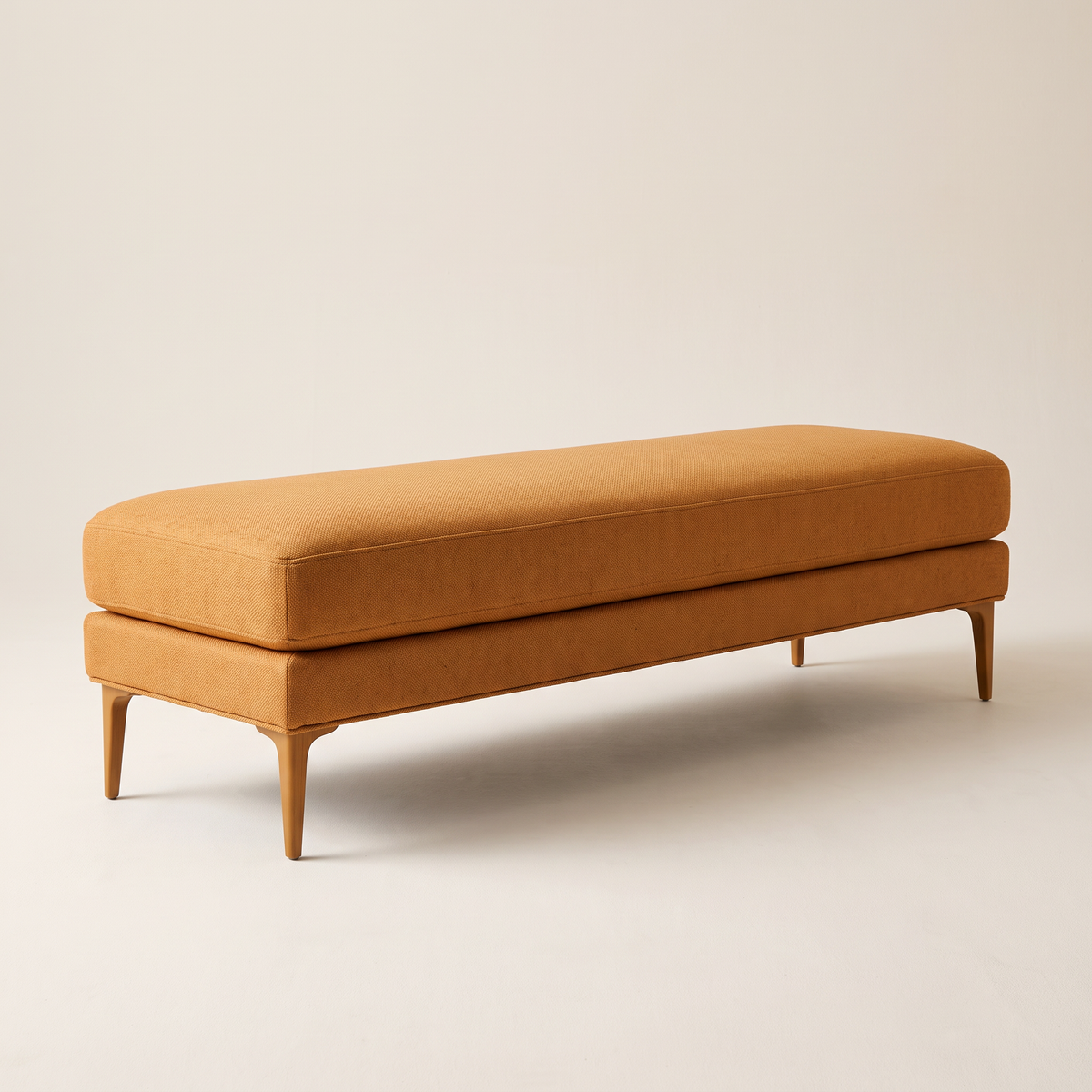 Amber Muse ottoman bench in amber woven fabric with slim tapered wooden legs, front three-quarter view
