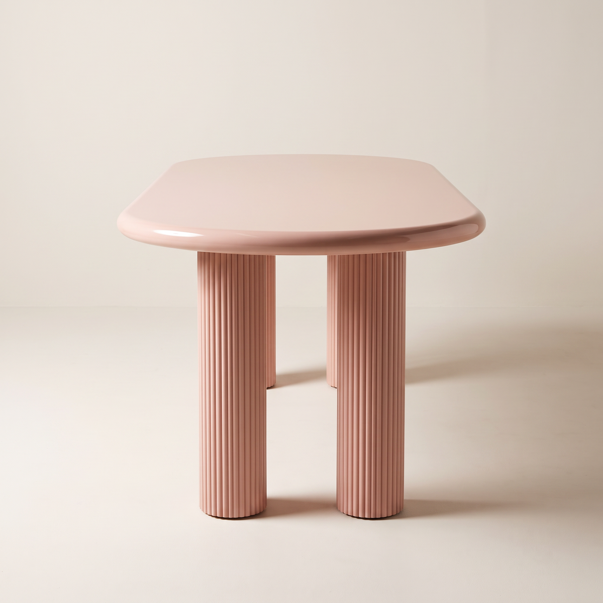 Aurelia dining table with blush-pink gloss racetrack top on four fluted column legs, end view