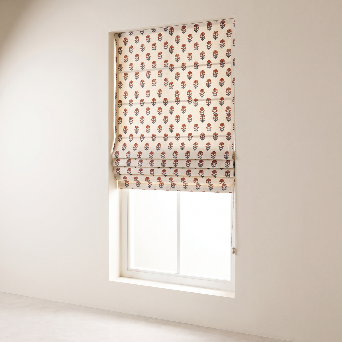 Bagh Roman Blind in ivory hand block-printed cotton with rust and indigo floral buti, half raised in four folds, front three-quarter view