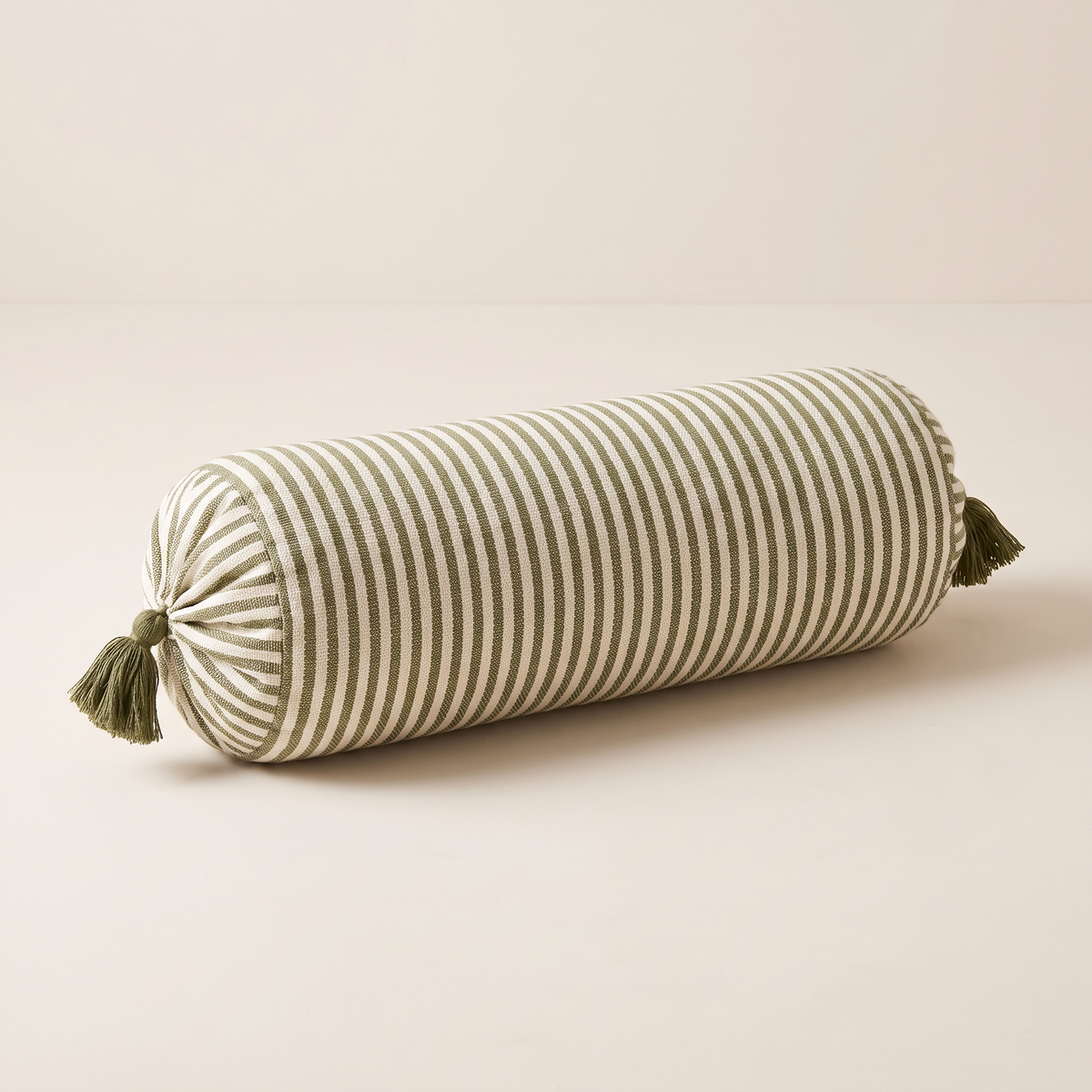 Bolster Stripe cylindrical cushion in handwoven ivory and olive ring stripes with olive tassels, front three-quarter view