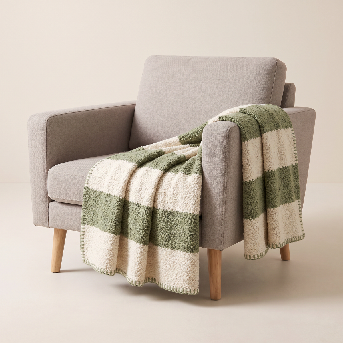 Bouclé Stripe Throw in wide ivory and sage bouclé bands with sage whipstitch edge, draped over an armchair, front three-quarter view