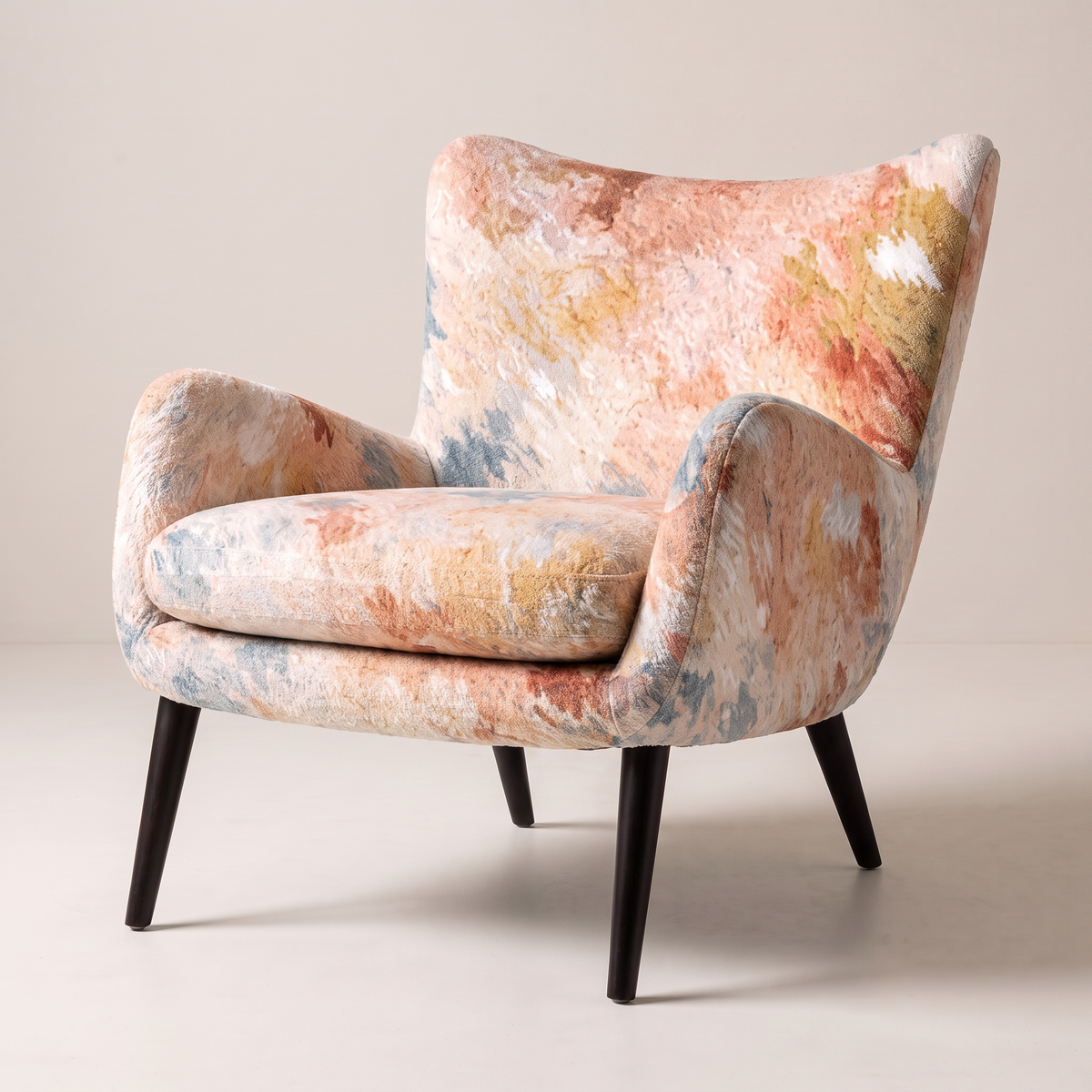 Canvas Fresco wingback lounge chair in painterly peach, coral and blue watercolour print with black tapered legs, front three-quarter view