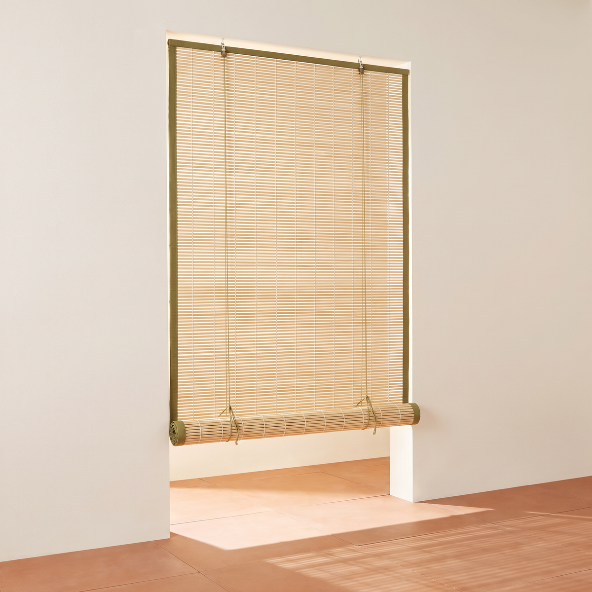 Chik Bamboo Blind in natural split bamboo with olive cotton tape edging, partly rolled up with cords, front three-quarter view