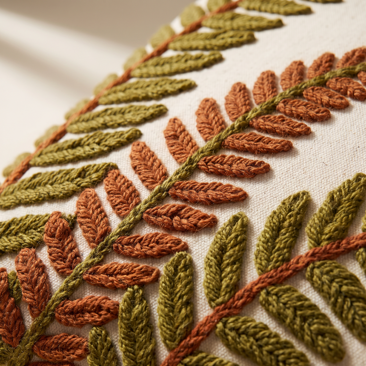 Close-up of Crewel Fern Cushion showing raised wool chain-stitch fronds in olive and rust