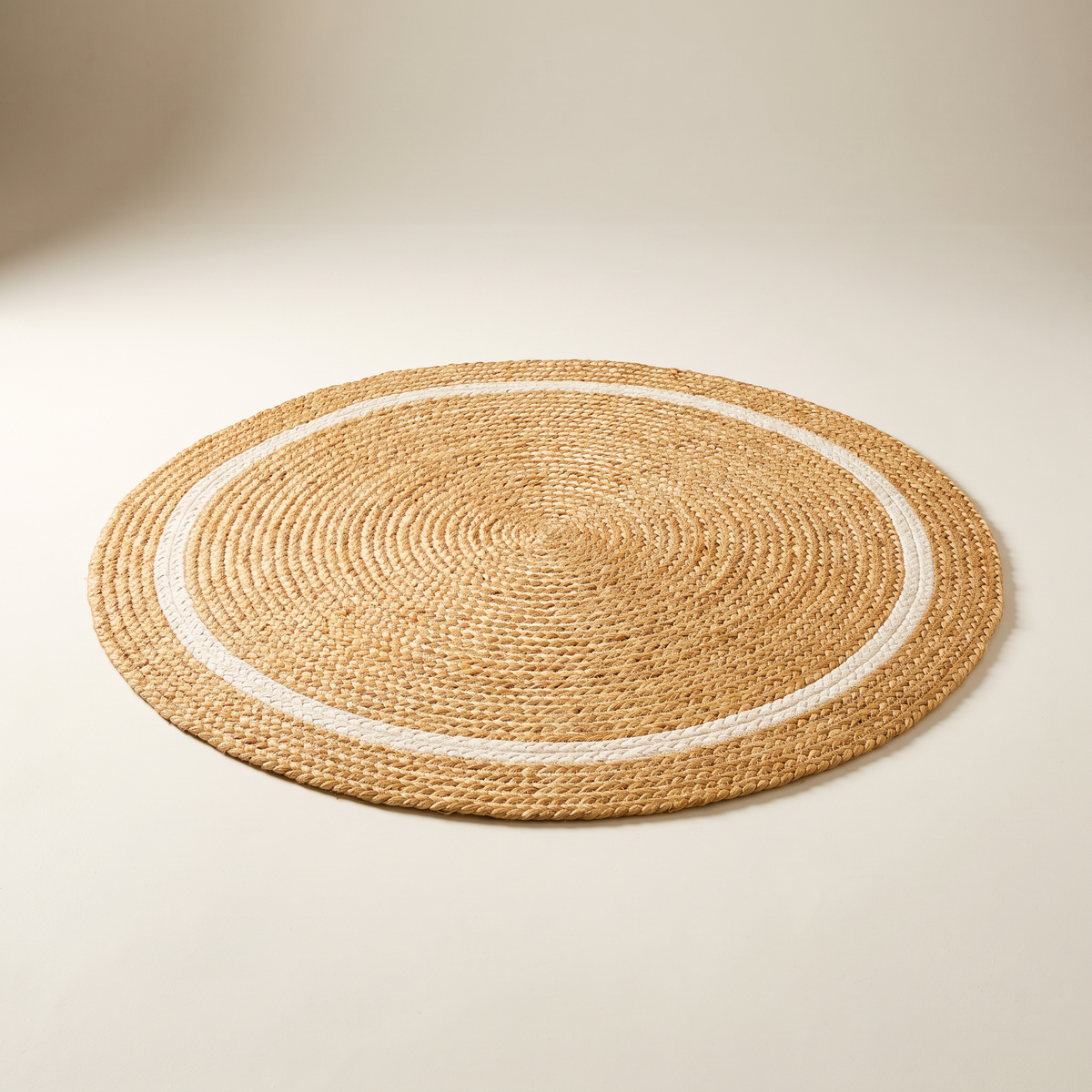 Disc Jute Round, braided natural jute round rug with one ivory cotton ring, elevated three-quarter view