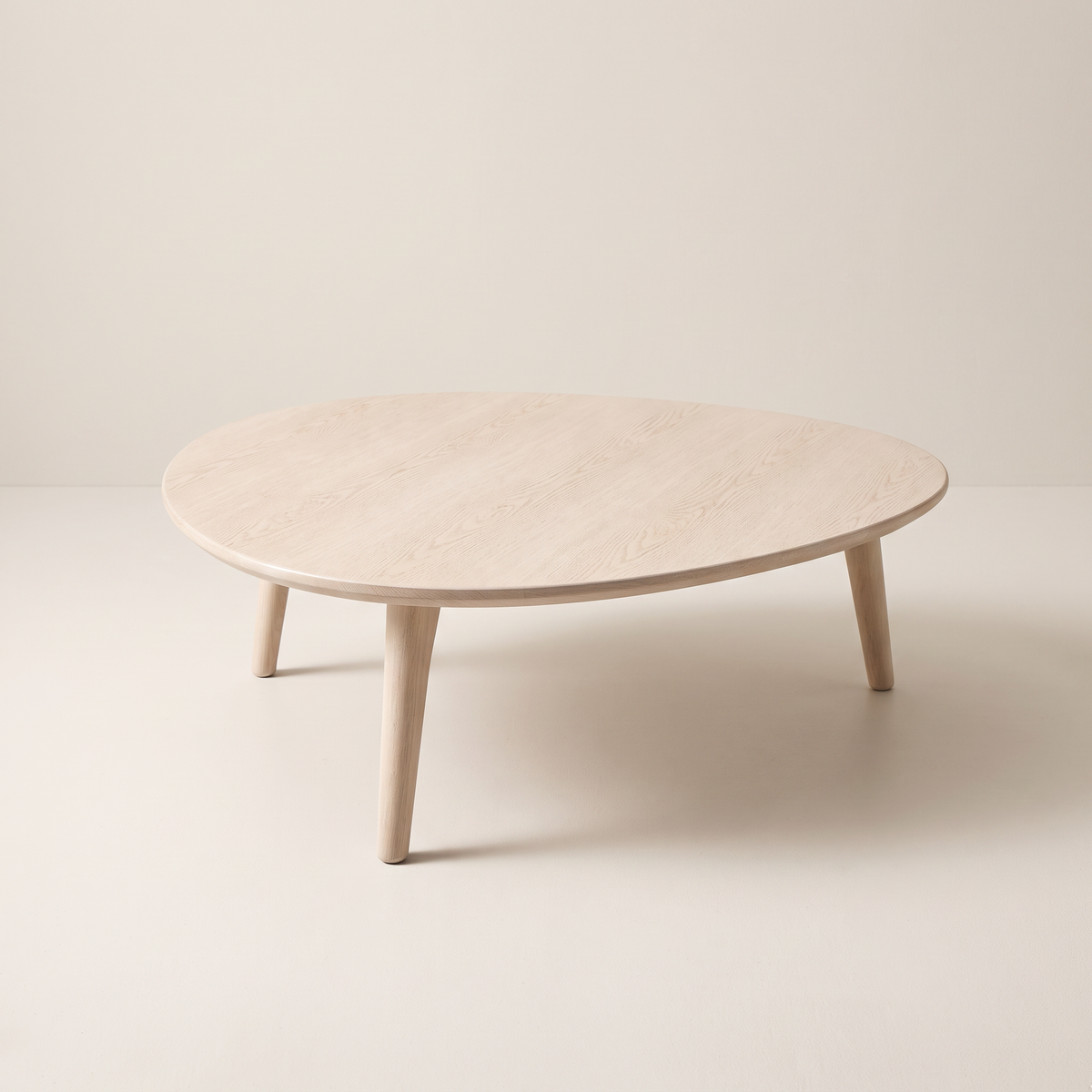 Eira Ash coffee table with pebble-shaped pale ash wood top and three tapered legs, front three-quarter view