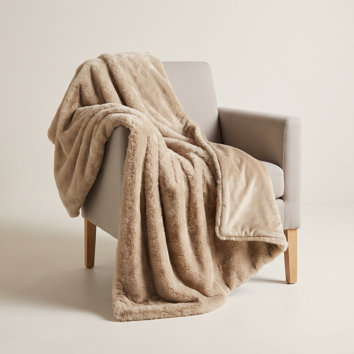 Faux Fur Throw in warm oat long-pile faux fur with oat velvet back, draped over an armchair, front three-quarter view