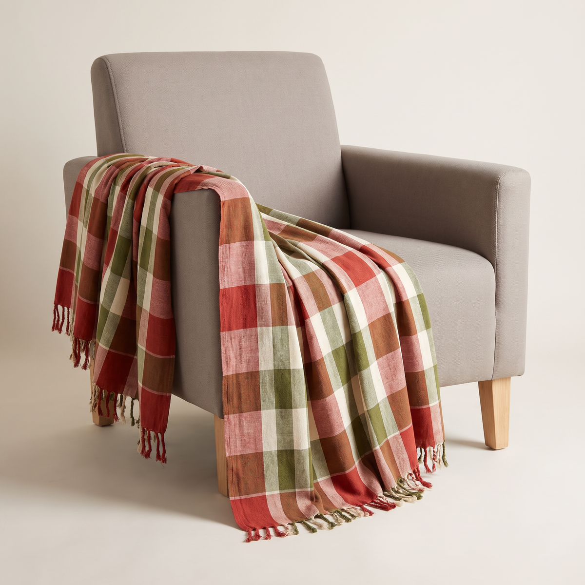 Gamcha Check Throw in brick red, ivory and olive handloom cotton check with short fringe, draped over an armchair, front three-quarter view