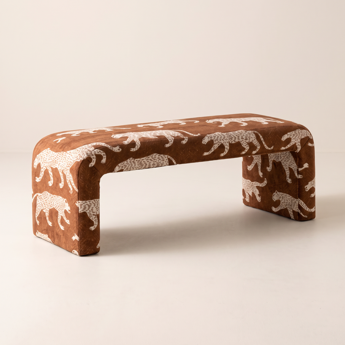 Glyph – Nomad waterfall bench in rust-brown fabric with cream walking-leopard print, front three-quarter view