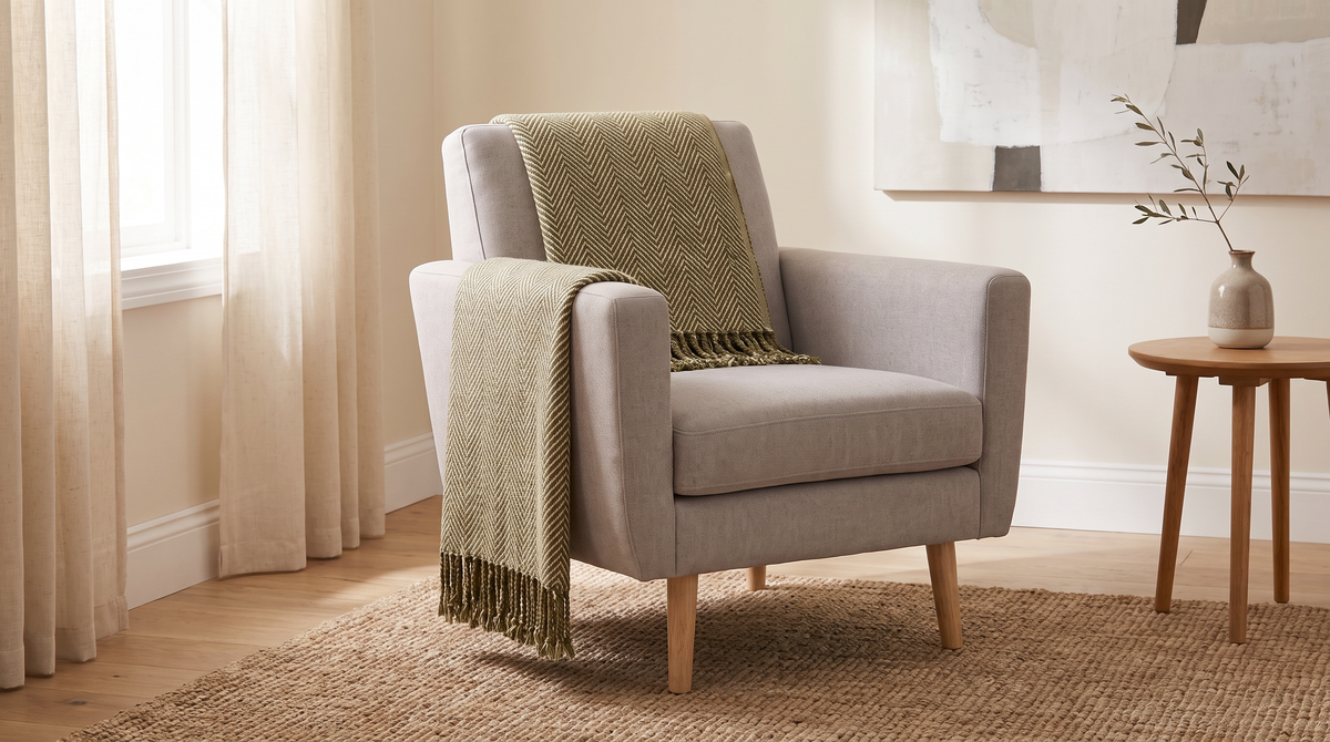 Herringbone Fringe Throw in olive and cream on a neutral armchair in a calm living room