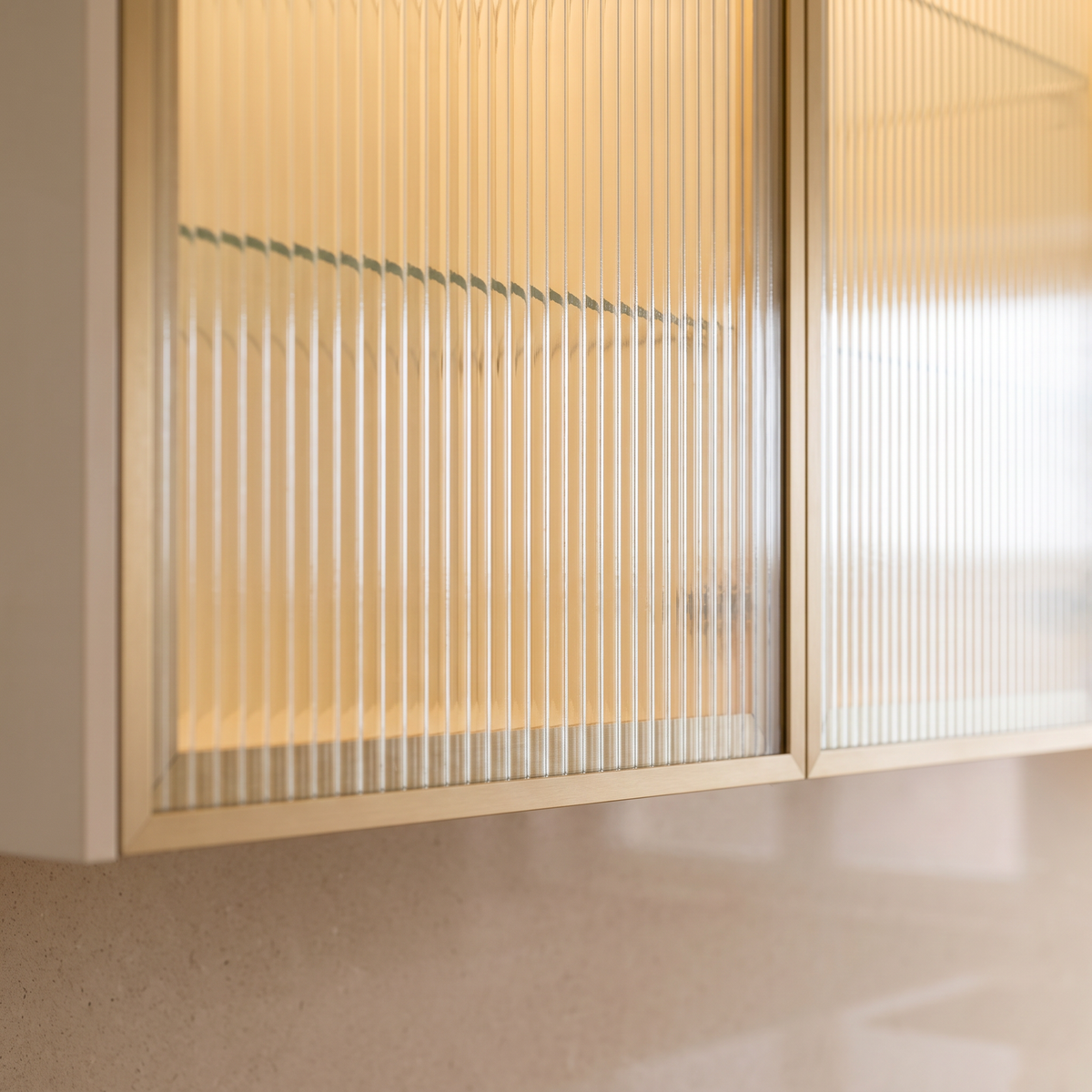 Juniper Galley detail of a reeded frosted-glass wall cabinet door in a champagne-gold frame with warm interior light