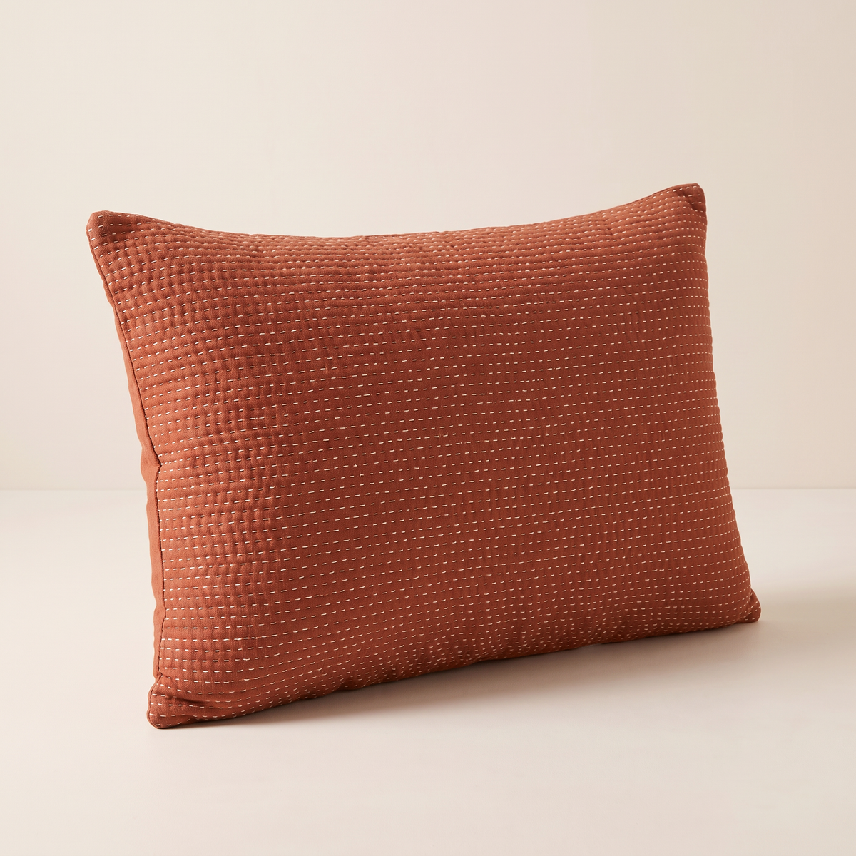 Kantha Lumbar cushion in rust cotton with rows of cream kantha running stitch, front three-quarter view