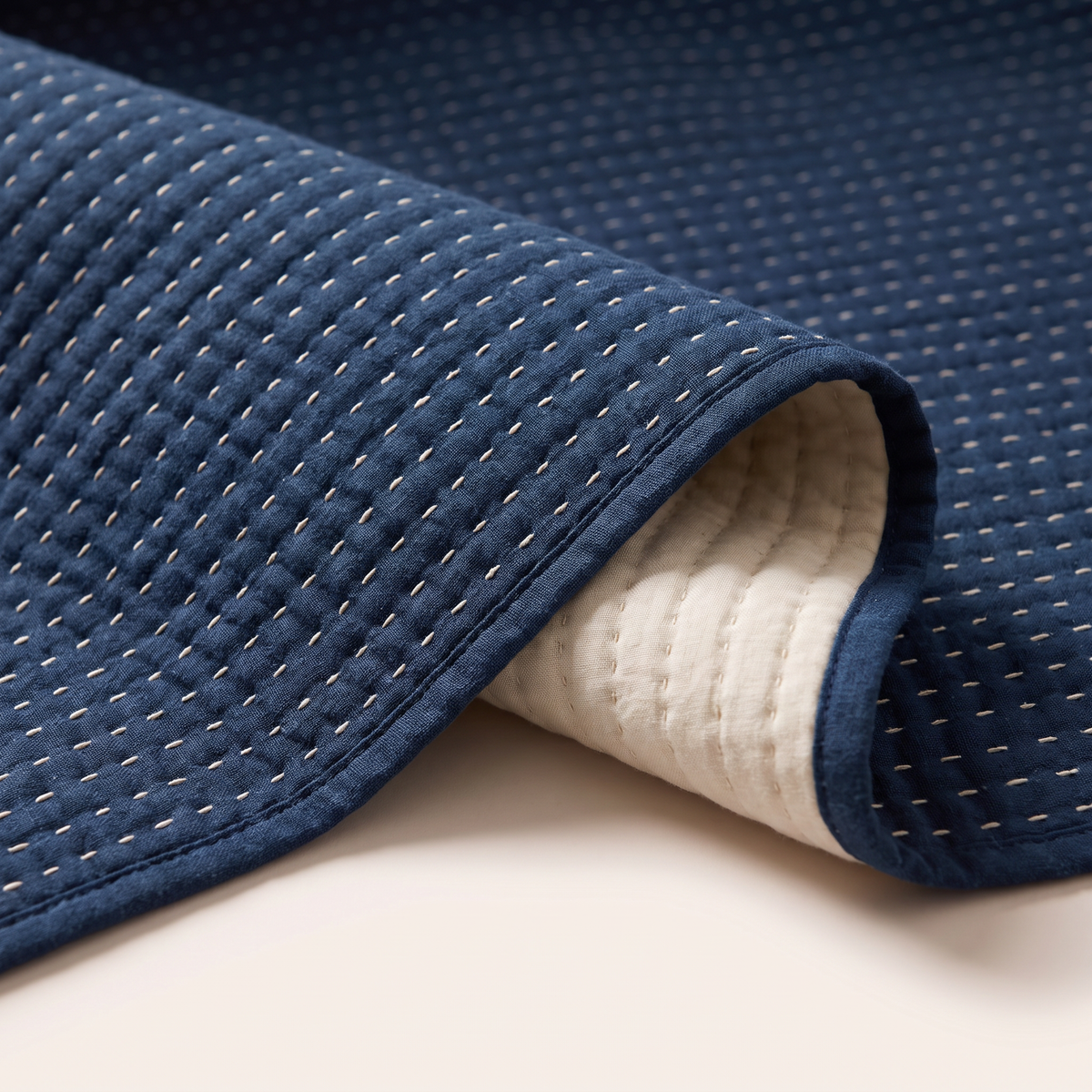 Close-up of Kantha Quilted Coverlet ivory running stitches on indigo cotton with the plain ivory reverse