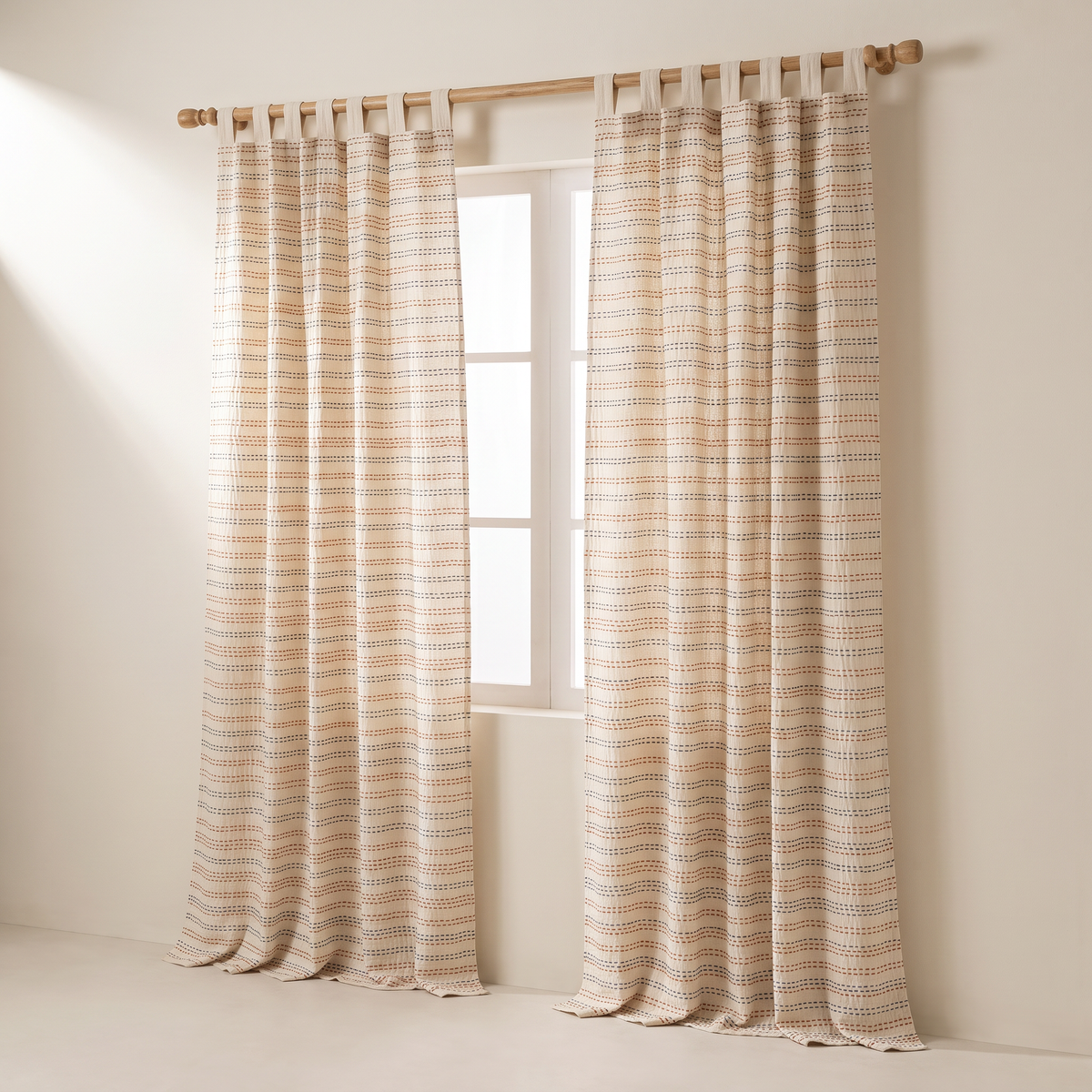 Kantha Stitch curtains in ivory cotton with rows of rust and indigo running-stitch embroidery, tab-top on a wooden rod, front three-quarter view