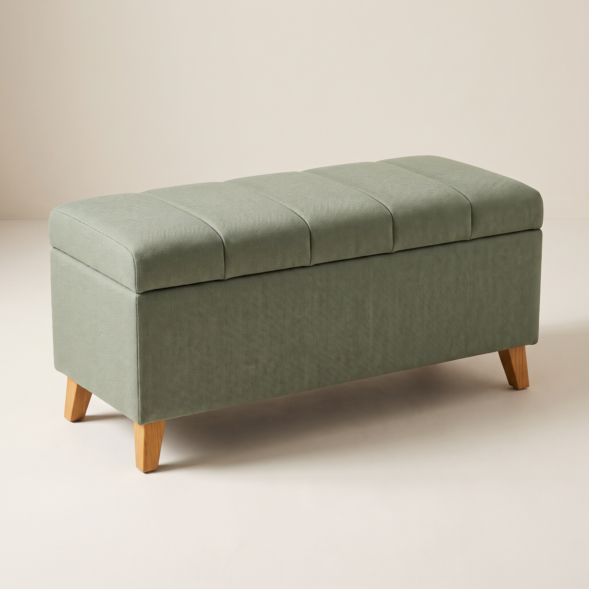 Keel Storage Bench in woven sage fabric with channel-stitched padded lid on tapered ash legs, front three-quarter view