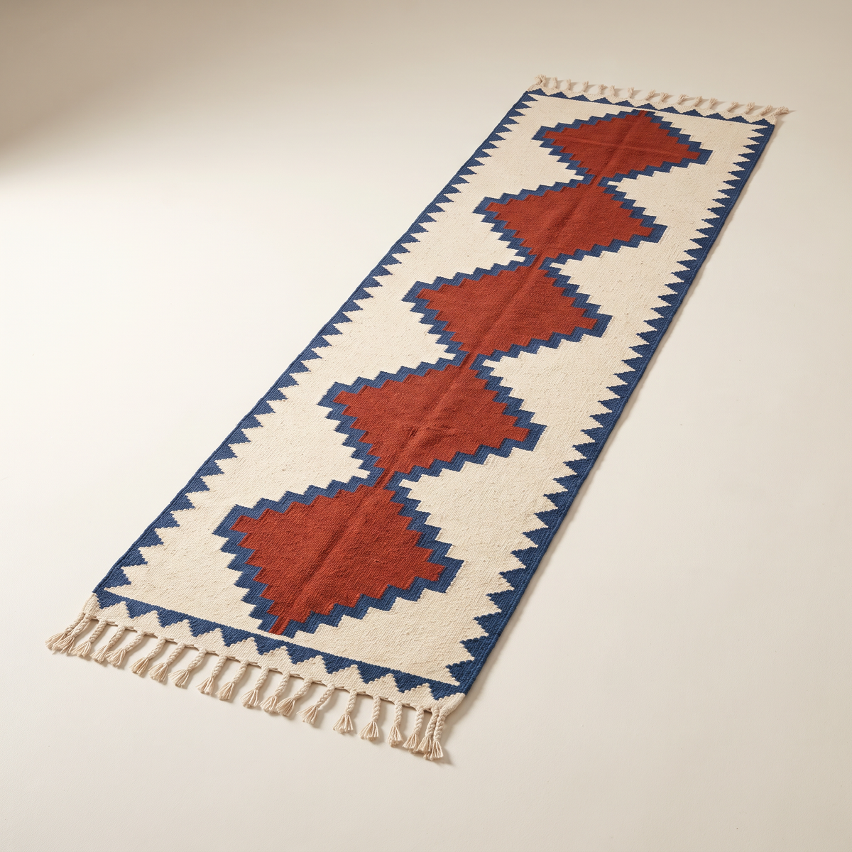 Kilim Runner, flatwoven wool with rust diamonds outlined in indigo on cream and braided tassels, elevated three-quarter view
