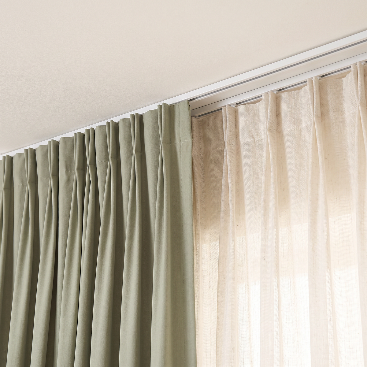 Close-up of Layer Pair Set pinch-pleat headings on a double track, sage cotton beside translucent ivory sheer