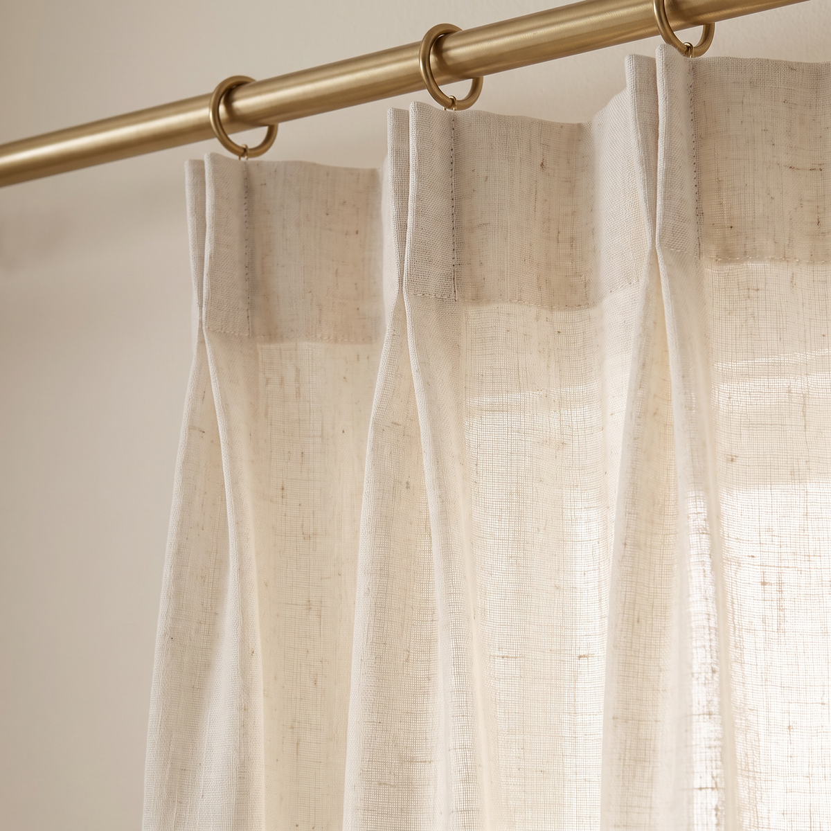Close-up of Mist Linen Sheer pinch-pleat heading, brass rings and slubbed linen-blend voile with light filtering through