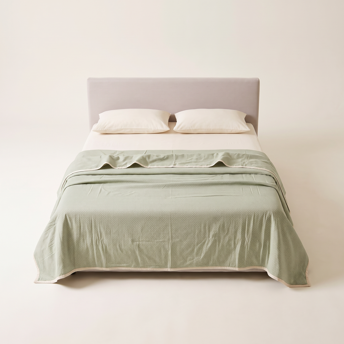 Mulmul Dohar sage dot print with ivory binding on a bed, view from the foot