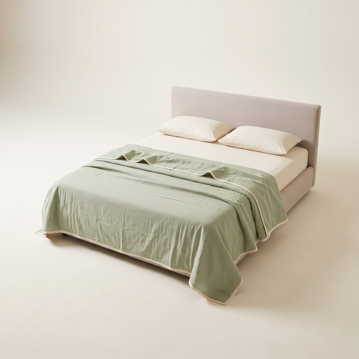 Mulmul Dohar in pale sage cotton mulmul with tiny ivory dots and ivory binding, on a low studio bed, front three-quarter view