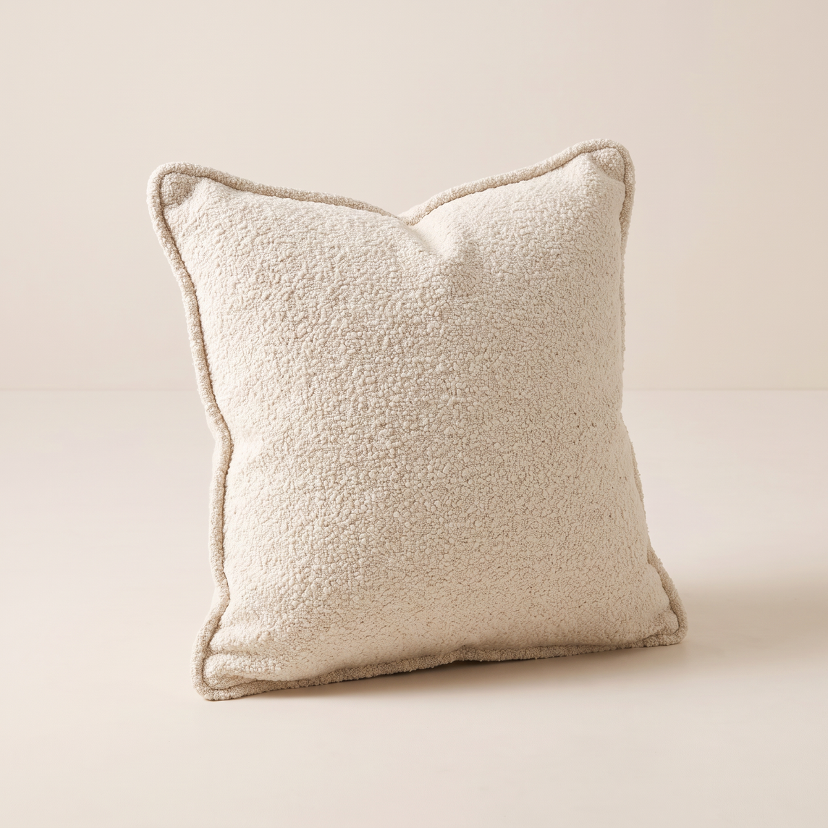 Nimbus Bouclé Cushion in ivory-cream bouclé with self-fabric piping, front three-quarter view