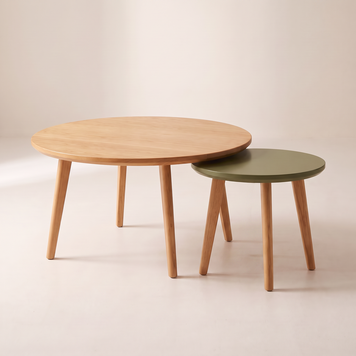 Orbit Nest round nesting coffee tables: honey ash table on three splayed legs with smaller olive lacquer table on four splayed ash legs, front three-quarter view