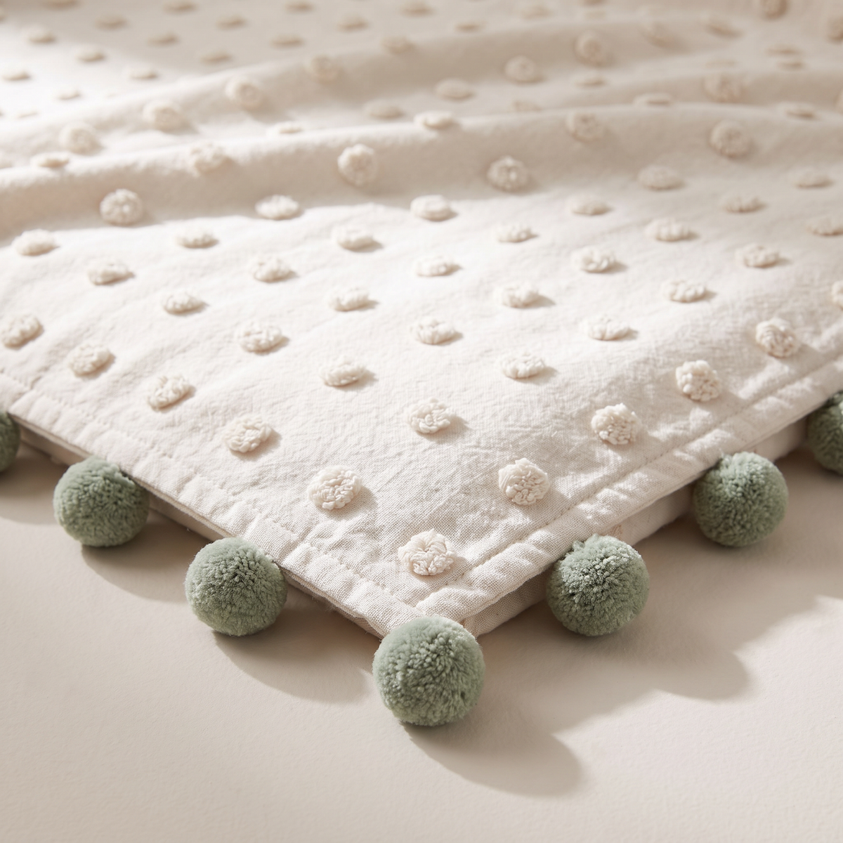 Pom-Pom Tufted Throw close-up of the raised ivory tufted dots and sage pom-poms