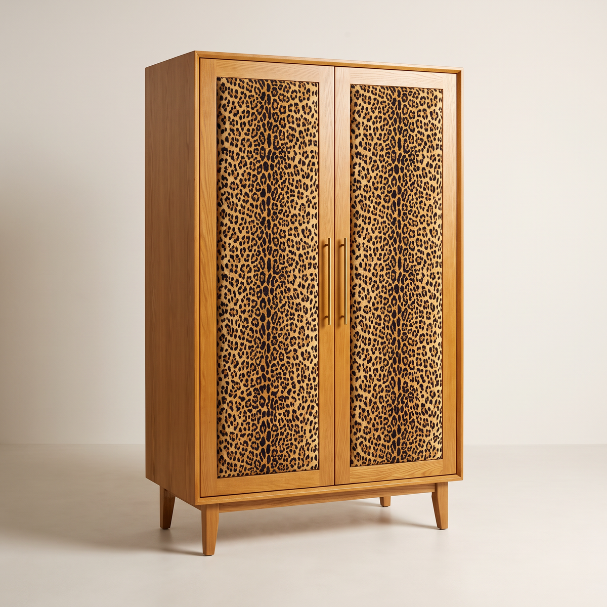 Prowl Wardrobe with padded leopard-print door panels in honey ash frames, brass handles and tapered ash legs, front three-quarter view