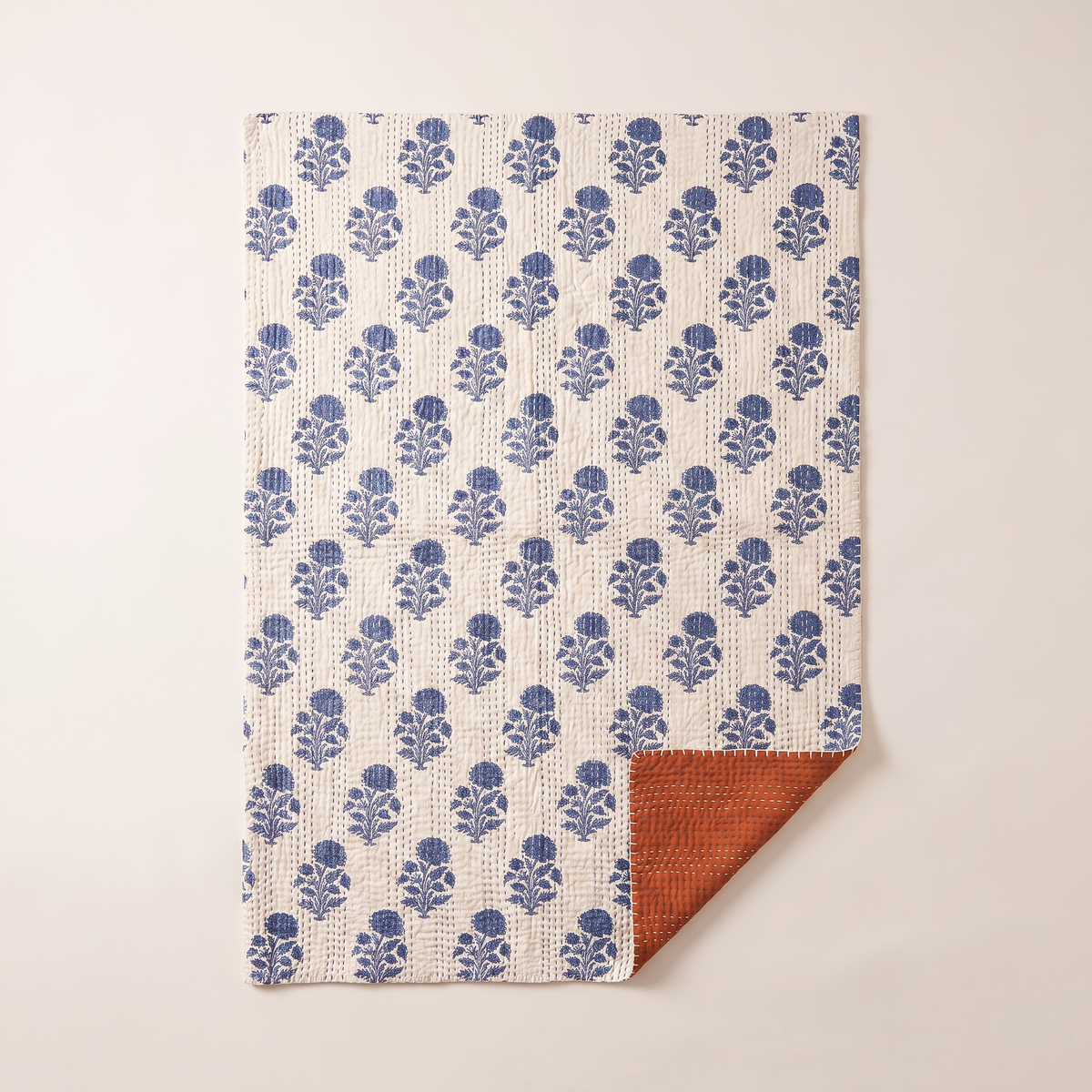 Reversible Kantha Throw spread flat, overhead view of the indigo floral face with one corner folded to the rust reverse