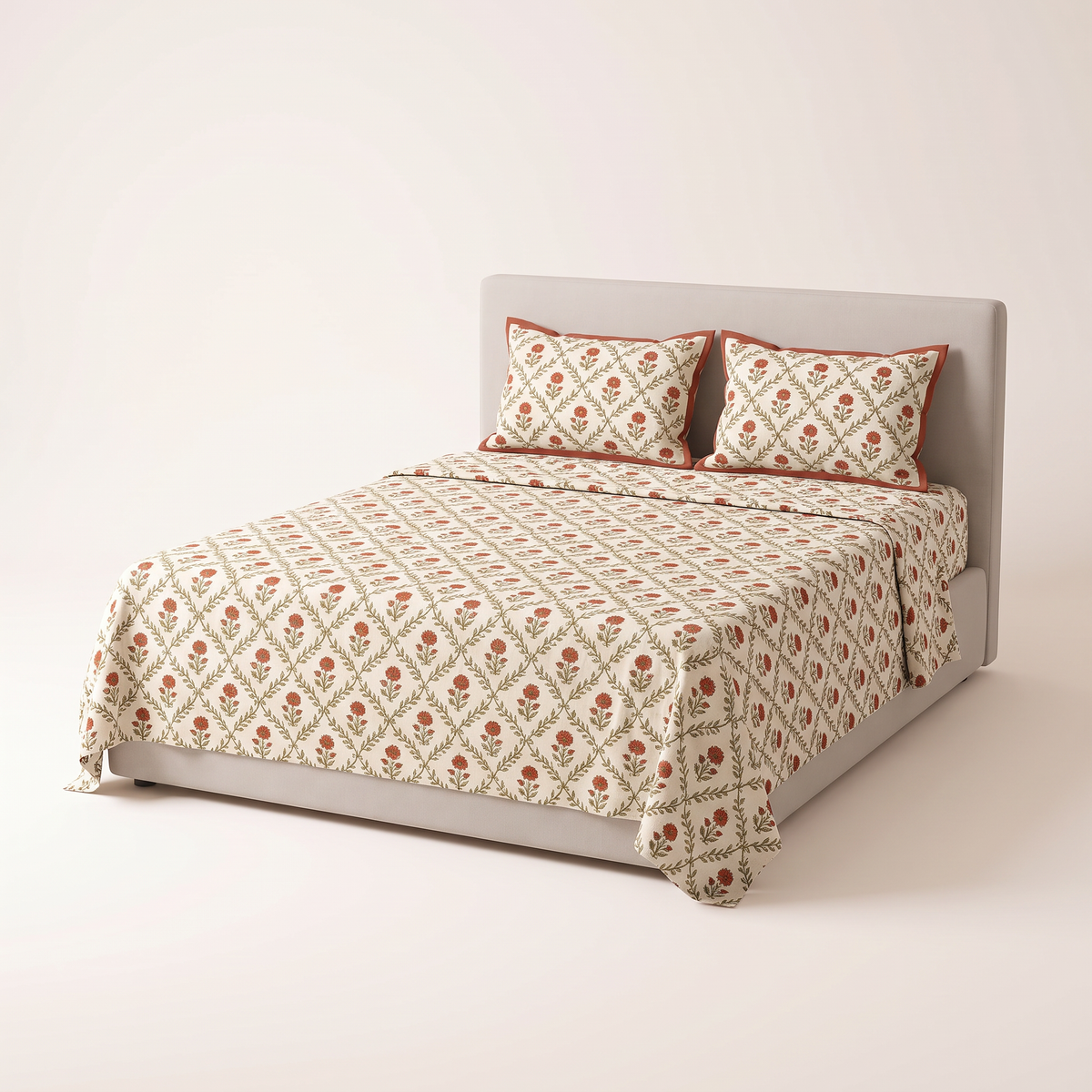 Sanganer Block Sheet Set in ivory cotton block-printed with a rust floral and olive vine jaal, pillow covers with rust border, on a low studio bed, front three-quarter view