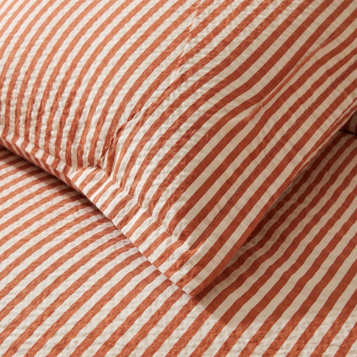 Close-up of Seersucker Stripe Set puckered rust and ivory stripes on sham and duvet