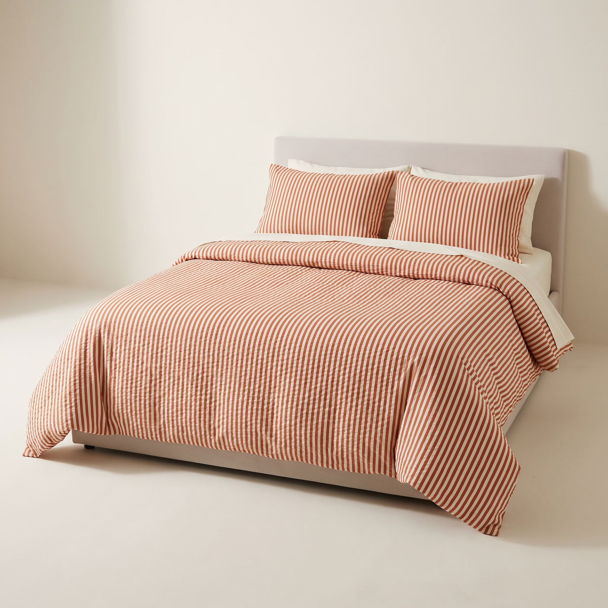 Seersucker Stripe Set duvet cover and shams in puckered cotton seersucker with narrow rust and ivory stripes, on a low studio bed, front three-quarter view