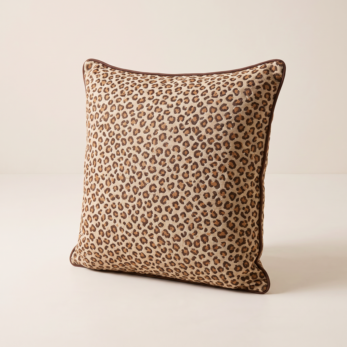 Spot Jacquard Cushion in caramel and chocolate leopard jacquard on sand with chocolate piping, front three-quarter view