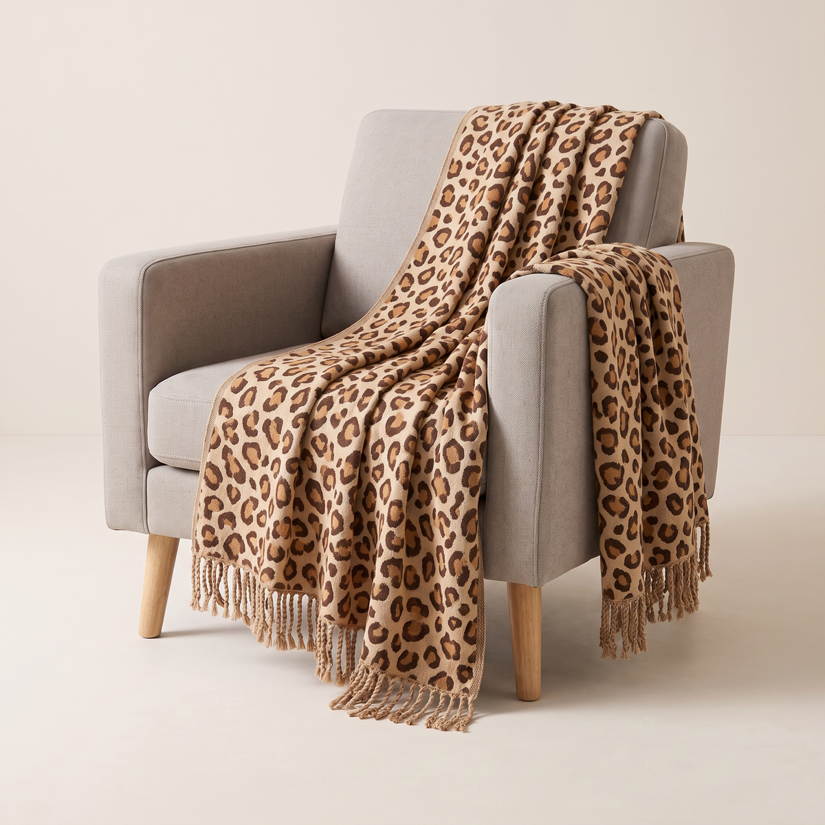 Spotted Fringe Throw in caramel and chocolate leopard cotton jacquard on sand with knotted fringe, draped over an armchair, front three-quarter view