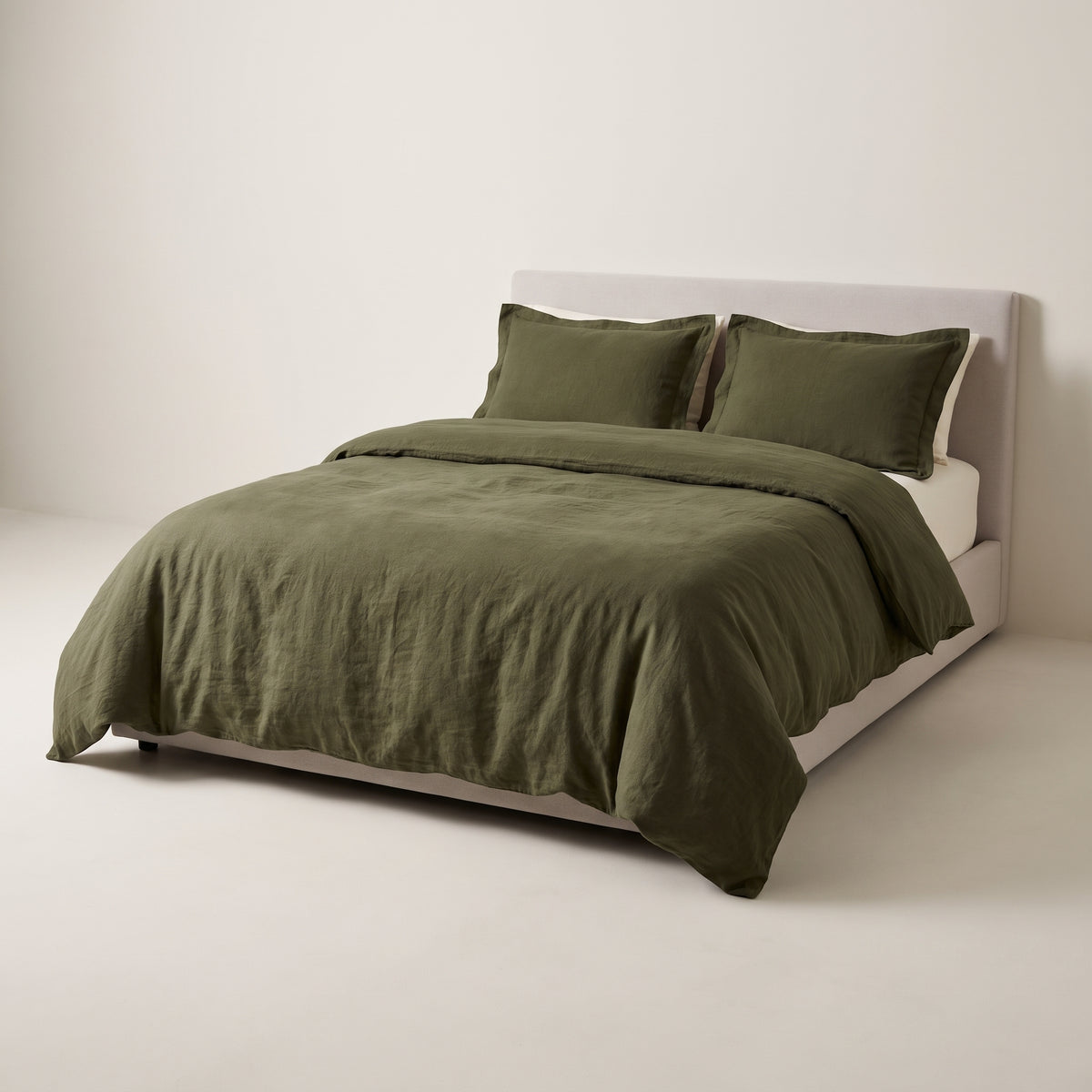 Stonewash Olive Duvet Set in rumpled deep olive linen-cotton with two flanged shams, on a low studio bed, front three-quarter view