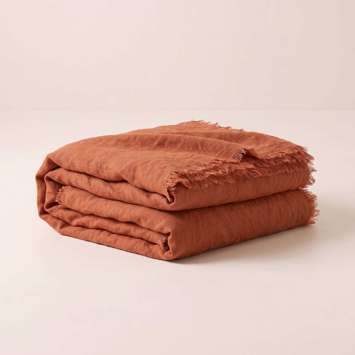 Stonewashed Linen Throw in rust linen, folded with frayed edges showing