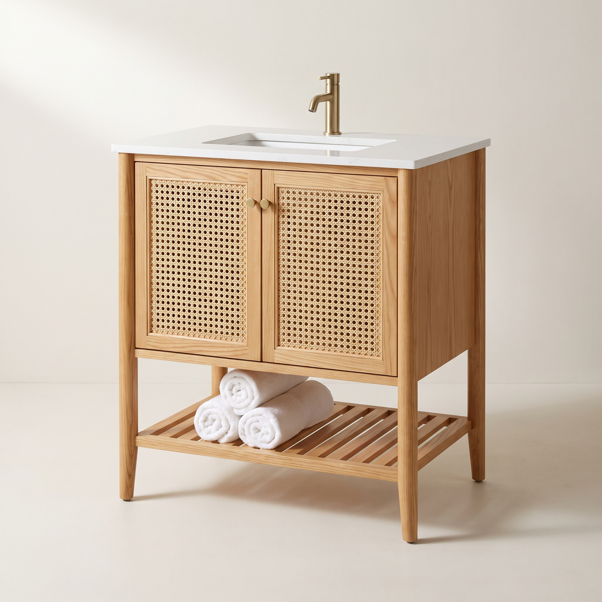 Tala Cane Vanity in honey ash with two woven cane doors, brass knobs, slatted towel shelf, tapered legs and white quartz top with undermount basin, three-quarter studio view