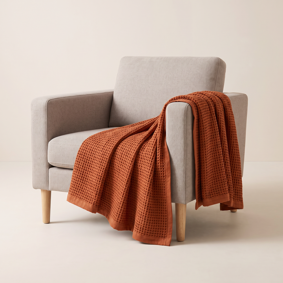 Waffle Cotton Throw in rust cotton waffle weave with plain hem, draped over an armchair arm, front three-quarter view
